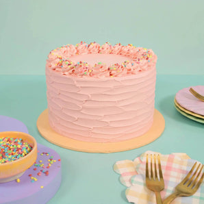 Vegan Vanilla Cake by Crumbs & Doilies with pink vegan buttercream icing and colorful sprinkles on top.